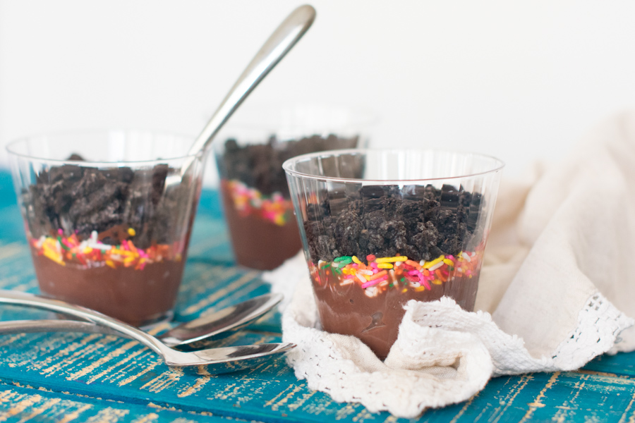 Clear plastic cups filled with pudding, rainbow sprinkles, and crushed oreo cookies