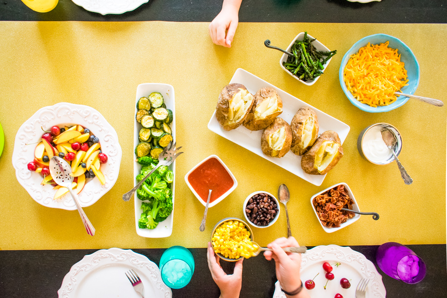 Overhead shot of children's hands filling baked potatoes with various toppings. 