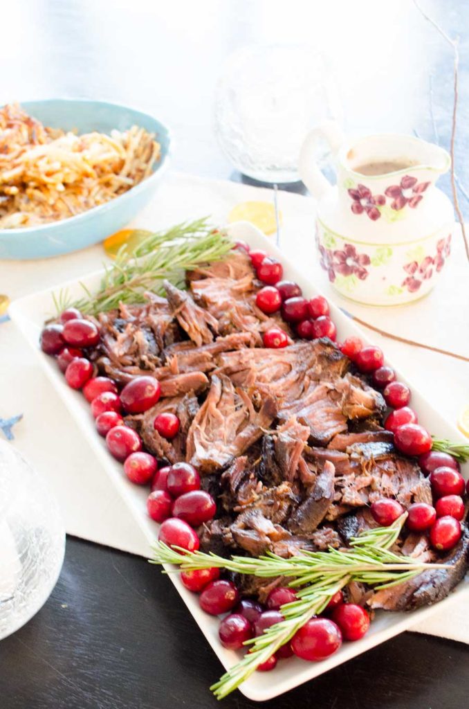 Braised short ribs on a platter with fresh cranberries and rosemary. 