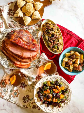 overhead shot of a table of food to celebrate the Winter Solstice. Spiral sliced ham, brussels sprouts, roasted potatoes, mixed beets, and apple cider.